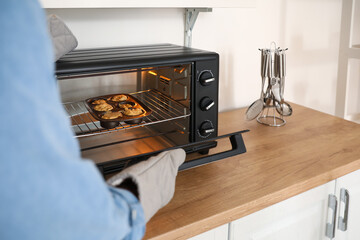 Young man putting raw peach muffins into oven in kitchen