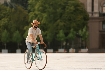 Handsome bearded man riding bicycle on city square