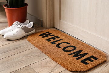 Mat with word WELCOME and male sneakers near light wooden door in hall, closeup