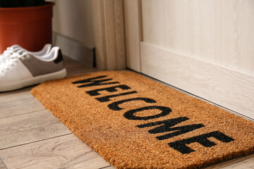 Mat with word WELCOME near light wooden door in hall, closeup - obrazy, fototapety, plakaty