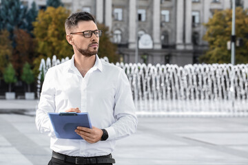 Stylish businessman writing in clipboard on city square