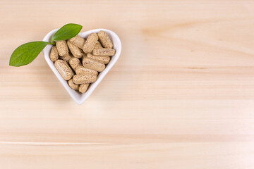 Herbal pills in heart shaped plate and green leafs on blue background.
