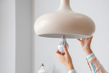 Woman changing light bulb in hanging lamp at home, closeup