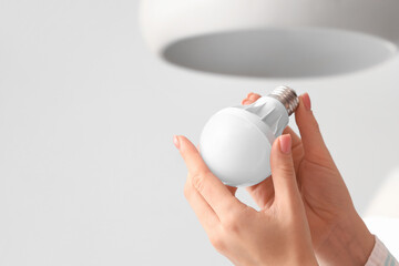 Woman changing light bulb in hanging lamp at home, closeup