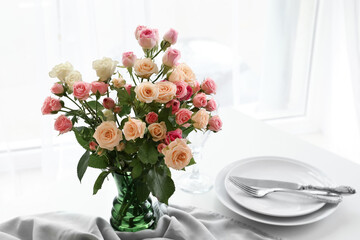 Vase with beautiful roses on served table in light room