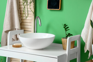 Table with white sink, houseplant and soap near green wall