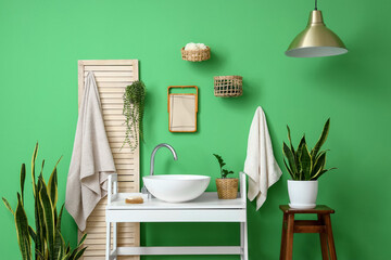 Interior of stylish bathroom with white table, sink and houseplants