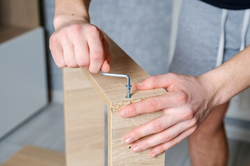 Close-up hands of unrecognizable craftsman using screwdriver and screw for assembling wooden furniture drawer during renovation in home