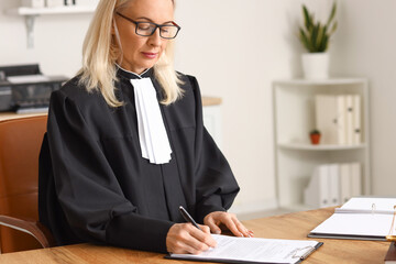 Mature female judge working with document at table in courtroom