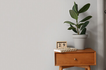 Wooden table with houseplant, book and cube calendar near light wall
