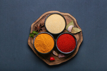Wooden board with bowls of aromatic spices on dark background