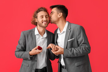Happy engaged gay couple on red background
