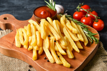 Wooden board with tasty french fries on black background