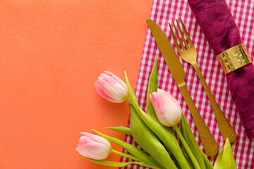 Stylish cutlery with tulip flowers on coral background