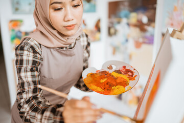 concentrated asian muslim female artist painting on canvas