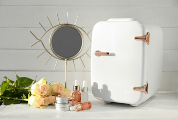 Small refrigerator with cosmetic products and flowers on table