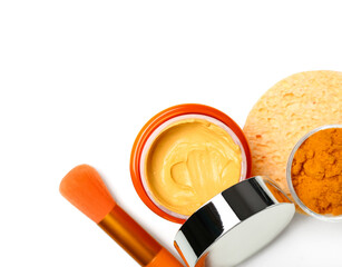 Jar with turmeric mask, powder and makeup brush on white background