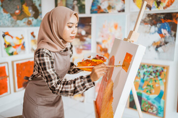 concentrated asian muslim female artist painting on canvas