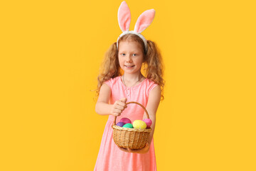 Funny little girl with bunny ears and Easter basket on color background