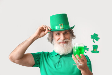 Senior man in green hat with beer on light background. St. Patrick's Day celebration