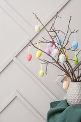 Vase with tree branches and Easter eggs on table near grey wall, closeup