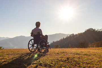 Male sitting on wheelchair looking sunset on mountain park. Silhouette