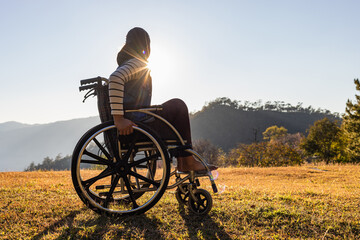 Female sitting on wheelchair looking sunset on mountain park. Silhouette