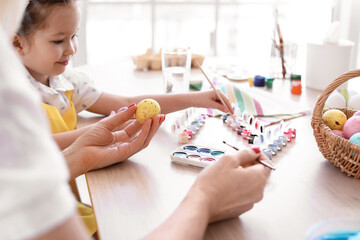 Little girl and her grandmother painting Easter eggs at home