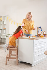 Little girl and her grandmother painting Easter eggs at home