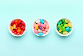 Bowls with different jelly beans on color background