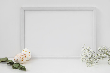 Composition with photo frame, Easter eggs, flowers and eucalyptus branch on table near light wall