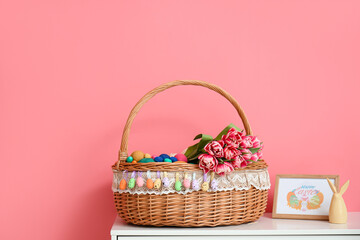 Fototapeta na wymiar Wicker basket with Easter eggs and flowers on table near color wall