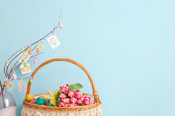 Vase and wicker basket with Easter eggs and flowers on blue background