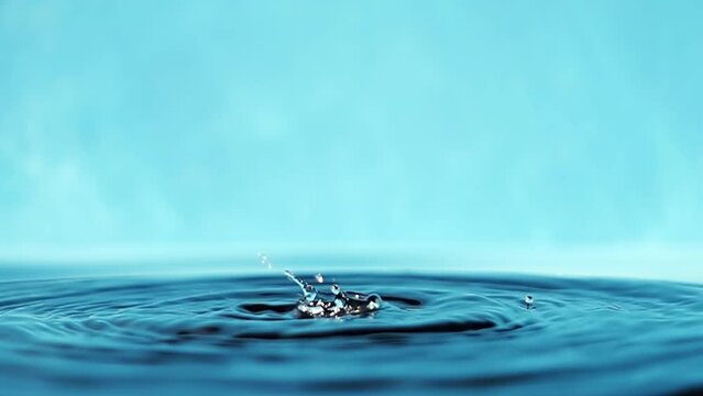 Water surface with falling drops on a blue background. Splashing water. Slow motion raw 4k video.