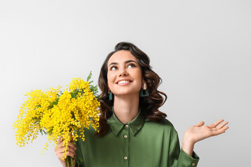 Beautiful young woman with mimosa flowers on light background - obrazy, fototapety, plakaty