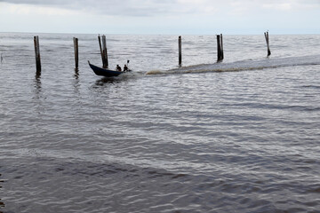 boat speeding cloudy rainy storm day rolling sea water wave on murky dirty rock sand shore jetty...
