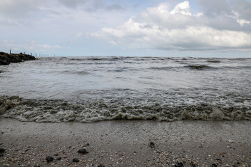 Fototapeta na wymiar cloudy rainy storm day rolling sea water wave on murky dirty rock sand shore