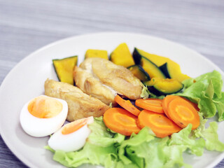 Clean meal and keto food with chicken, eggs and  seasoning with sesame sauce healthy for diet dining, eat with vegetables, carrot, beans and pumpkin. Put on the white plate isolated in grey table.