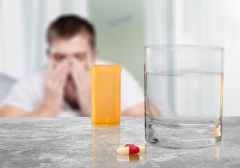 Tablets and a glass of water on the table in the background a sick person lies in bed. Taking medications