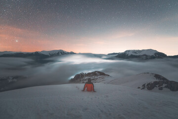 Climber sitting on the top of the snowy mountain and gazing the night sky