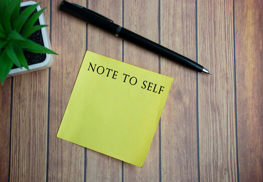 Note to self text on yellow stick note on wooden table