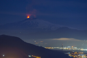 Eruption at Etna volcano at night time with sea and city lights in foreground seen from mainland on...