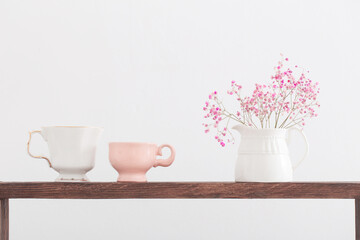 pink gypsophila and cups on  wooden shelf on  white background