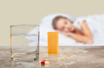Tablets and a glass of water on the table in the background a sick person lies in bed. Taking medications