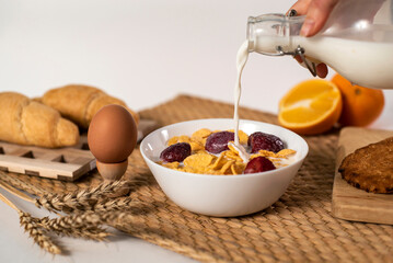 Hand of Woman Pouring Milk into a White Bowl with Cornflakes and Strawberries, Healthy Breakfast
