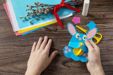 Obraz premium A child is holding an Easter bunny toy card with easter egg. Handmade. Project of childrens creativity, handicrafts, crafts for kids.