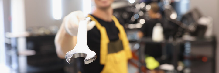 Uniformed car repairman holds wrench in car repair shop