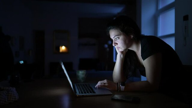 Woman browsing internet online looking at laptop screen at night
