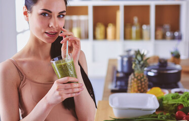 Young woman with glass of tasty healthy smoothie at table in kitchen