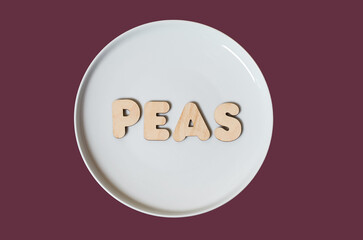 The word Peas made of wooden letters on a round white plate